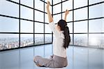 Businesswoman sitting cross legged cheering against room with large windows showing city