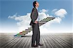 Serious businessman with hands on hips against book steps against sky