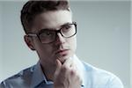 Close-up portrait of young man wearing eyeglasses and blue shirt, looking to the side, studio shot on white background