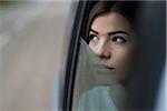 Portrait of young woman sitting inside car and looking out of window and day dreaming on overcast day, Germany