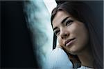 Portrait of young woman sitting inside car and looking out of window and day dreaming on overcast day, Germany