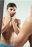 Close-up of young man reflected in bathroom mirror, holding face in hands, studio shot