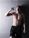 Young man pouring water over body after working out, studio shot on grey background