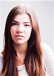 Close-up portrait of young woman with long, brown hair, serious expression and looking at camera, studio shot on white background