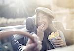 Young couple in convertible, woman eating chips