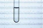 Test tube containing liquid with computer monitor displaying results of automated DNA sequencing