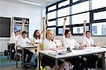 Group of schoolchildren with hands raised in classroom