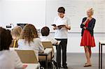 Schoolboy reading from textbook in front of class