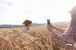 Mother photographing girl running through wheat field