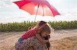 Mother and daughter hugging under red umbrella