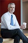 Businessman in waiting area of office, with hot drink