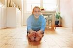 Young woman sitting on floor leaning forwards touching toes