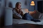 Young woman sitting on sofa, watching tv, eating chocolate