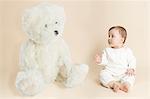 Studio portrait of baby girl next to giant teddy bear