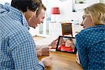 Grandmother and adult grandchildren looking at photo of baby boy on digital tablet