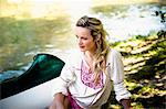 Young woman sits on the riverside, foothills of the Alps, Bavaria, Germany