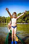 Boy in bathing trunks in a canoe, arms raised, Bavaria, Germany