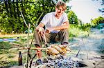 Young man barbecuing on the riverside, foothills of the Alps, Bavaria, Germany