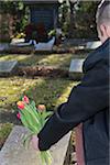 Backview of teenage boy placing flowere on grave stone in cemetery, Germany