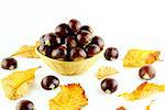 Sweet chestnuts in straw basket with leaves on white background.