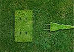 Green energy concept, Green power plug in electric outlet on a green grassland.