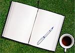 blank opened book outdoors on the green grassland with pen and tea cup.