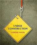 Alert yellow sign hanging by fishhook, conceptual image for under construction and coming soon