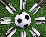 Football sport, soccer ball on grassland and knife and fork around.