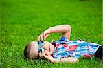 happy boy resting lying on green grass in sunglasses