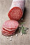 italian salami sausage slices with rosemary and sea salt, wood board