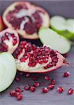 Pomegranate, pomegranate seeds and apple on a wooden board