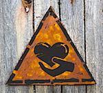 Charity. Icon of Heart in the Hand on Weathered Triangular Yellow Warning Sign. Grange Background.
