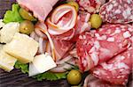 Arrangement of Delicatessen Cold Cuts with Smoked Ham, Various Sausages, Delicious Cheese and Green Olives closeup on Dark Wooden background