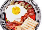 Tasty Breakfast with Fried Egg Sunny Side Up on Delicious Asparagus Sprouts, Roasted Bacon and Toasts on Striped Plate closeup on white background. Top View