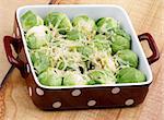 Delicious Brussels Sprouts Casserole with Grated Cheese and Spices in Brown Polka Dot Bowl closeup on Wooden background