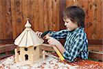Boy building a bird house - mounting the last roof piece with a nail and hammer