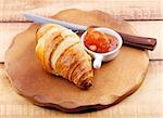 Freshly Baked Croissant with Apricot Jam and Table Knife on Wooden Plate closeup on Rustic Wooden background