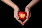 female teen hands holding apple with carved heart, isolated on black