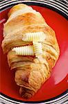 Freshly Baked Croissant with Slices of Butter closeup on Red Striped Plate