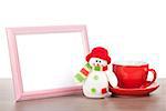 Blank photo frame, christmas snowman and coffee cup on wooden table. Isolated on white background