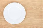 Empty white plate on wooden table. View from above