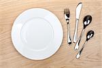 Empty white plate with silverware on wooden table. View from above