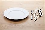 Empty white plate with silverware on wooden table