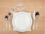 Empty plate, glasses and silverware set on wooden table