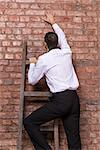 Man at the end of his search up against a brick wall standing balanced at the top of a stepladder, nowhere else to go