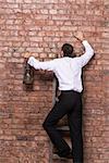 Man at the end of his search up against a brick wall standing balanced at the top of a stepladder with an old oil lamp in his hand with nowhere else to go