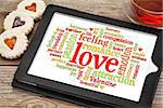 love word cloud on a digital tablet screen with heart cookies and a cup of tea