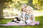 Sweet Little Girl Sitting with Her Baby Brother on a Picnic Blanket Outdoors at the Park.