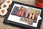 Happy birthday in letterpress wood type on digital tablet with stylus a cup of teat and heart cookies