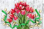 Easter eggs with red tulip flower arrangement and ribbon curl over distressed wooden background.